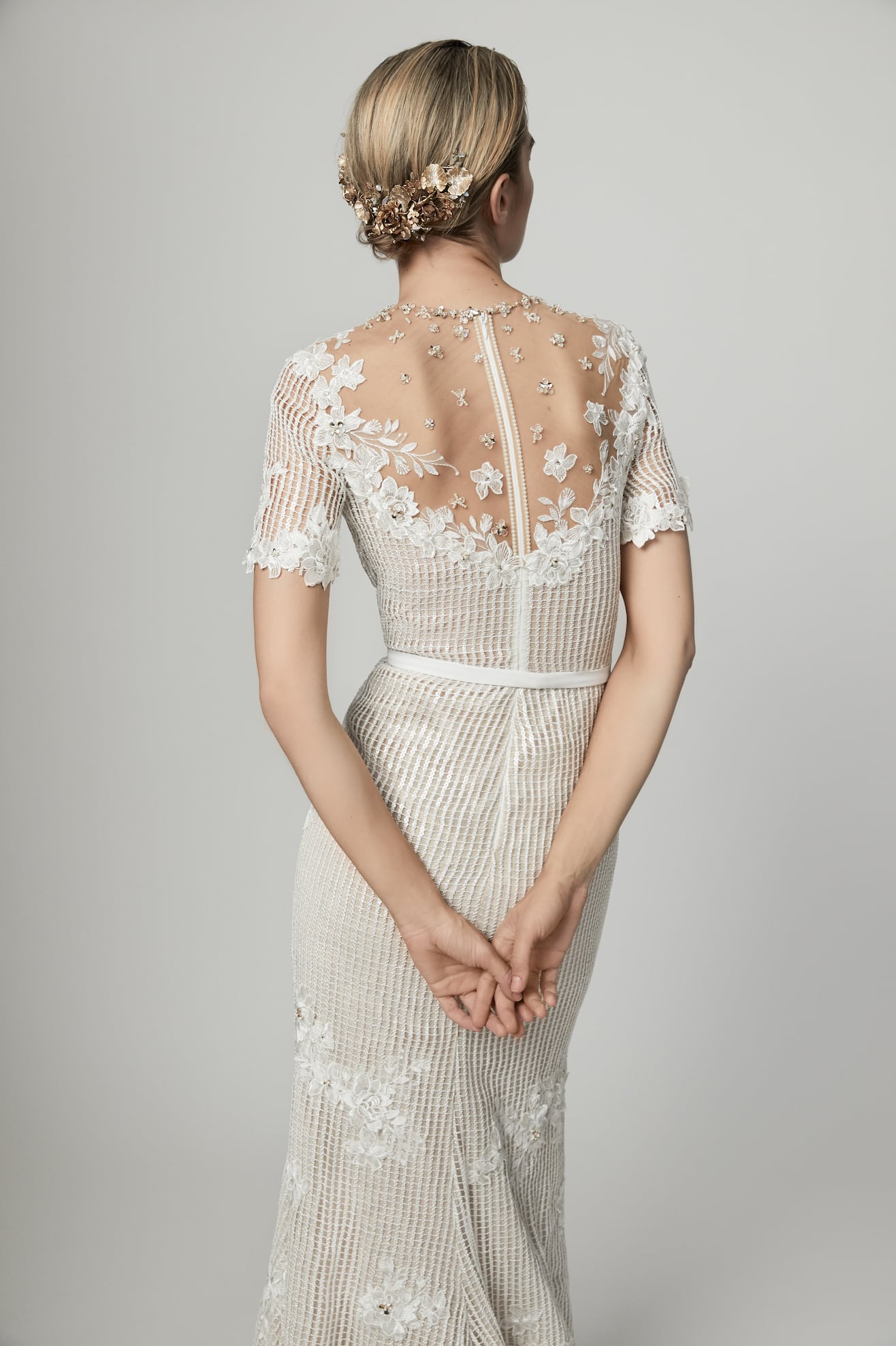 A woman in a mesh style dress with illusion back with floral appliqués from Our Story Bridal with her back to you 