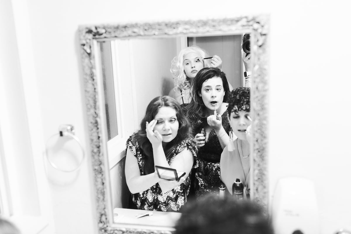 Four women getting ready for a party in a small bathroom with one mirror