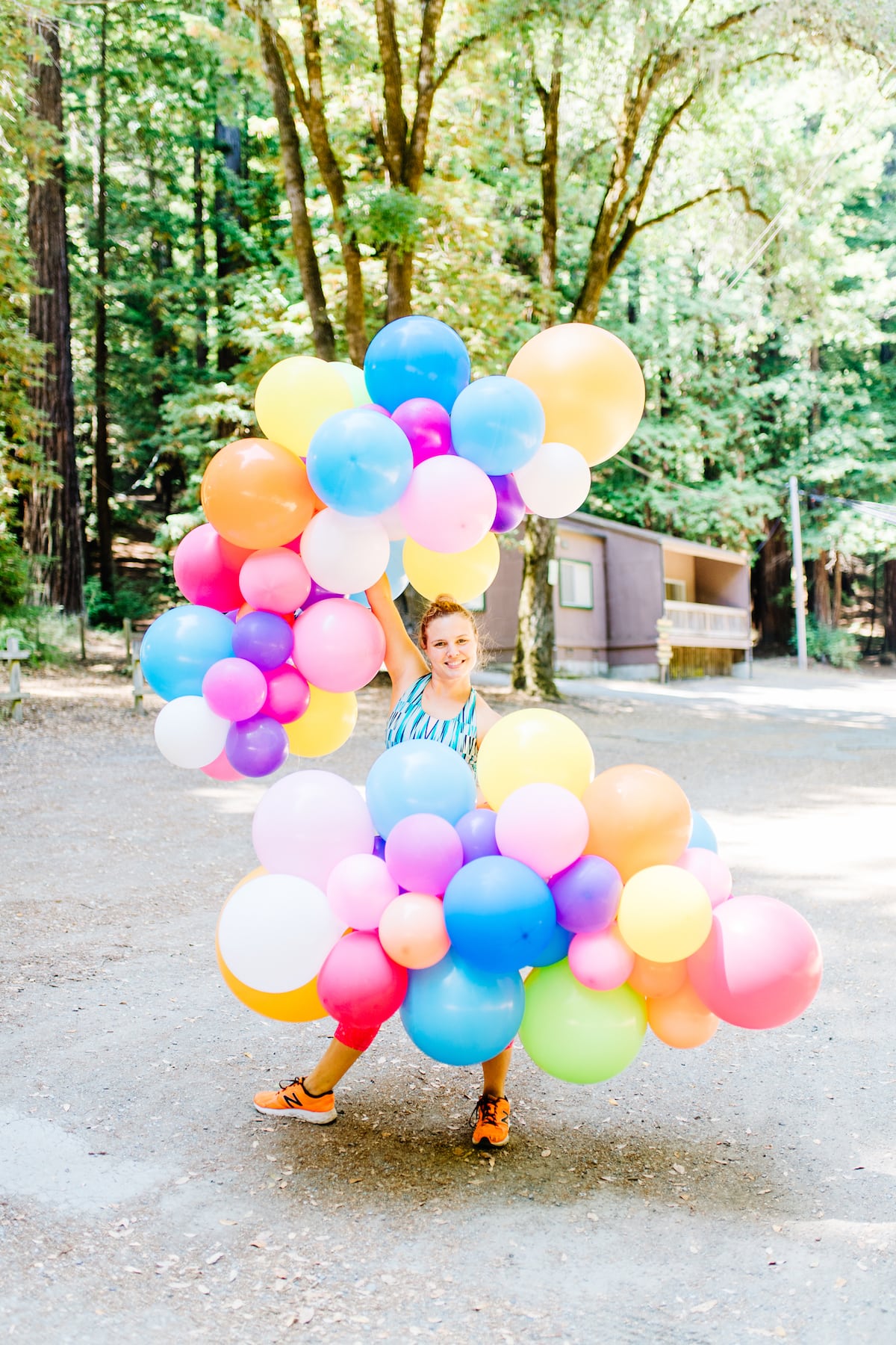 A woman holding a brightly colored ballon installation among the redwoods at the compact summer camp in la Honda, CA