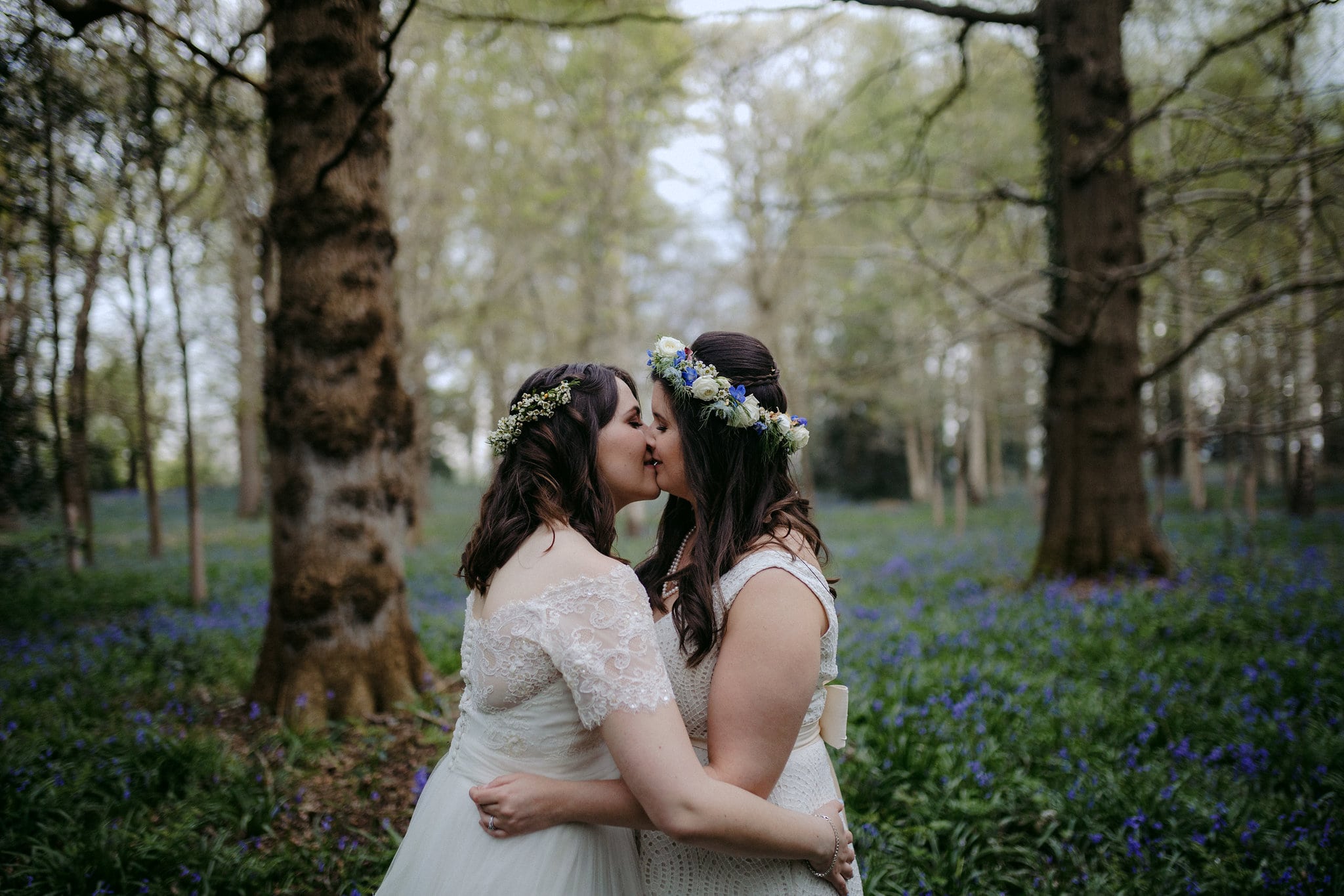 two brides kiss in the woods among blue flowers