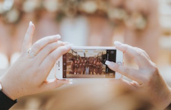 A photo of a line of bridesmaids on a smart phone screen, in the process of being taken by a woman with well manicured hands