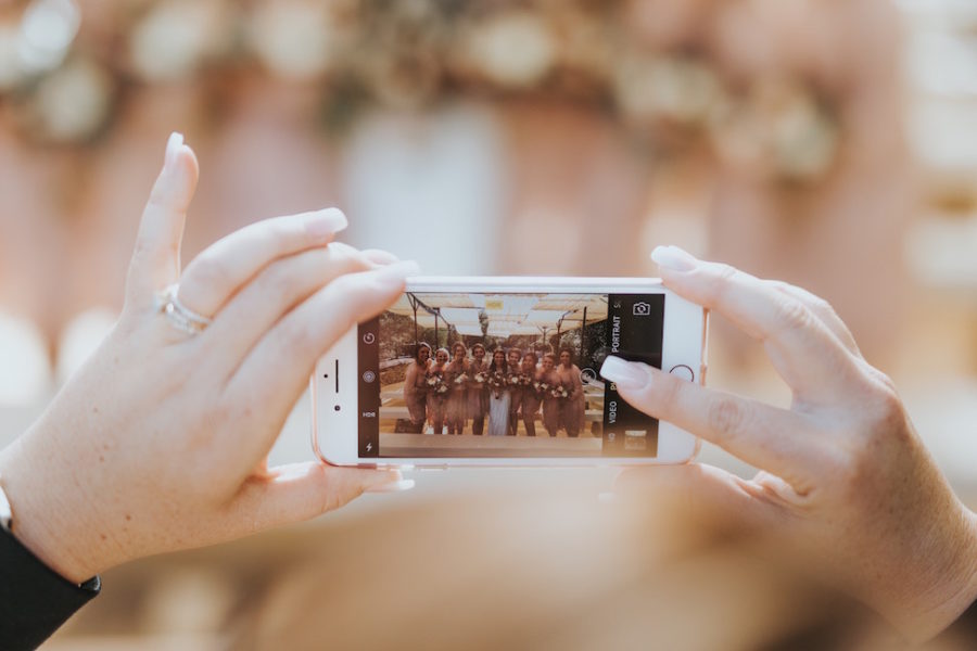 A photo of a line of bridesmaids on a smart phone screen, in the process of being taken by a woman with well manicured hands