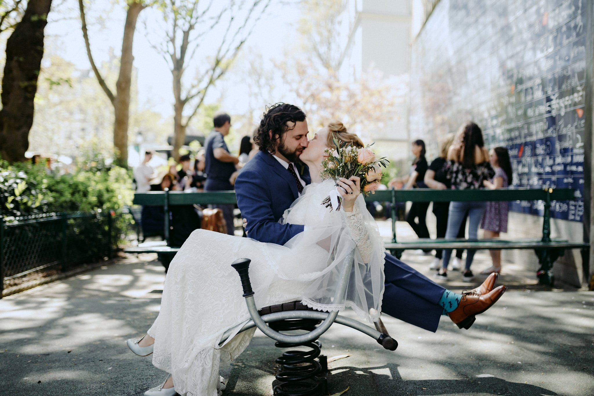 a wedding couple sits facing opposite directions on a bouncy bench, kissing