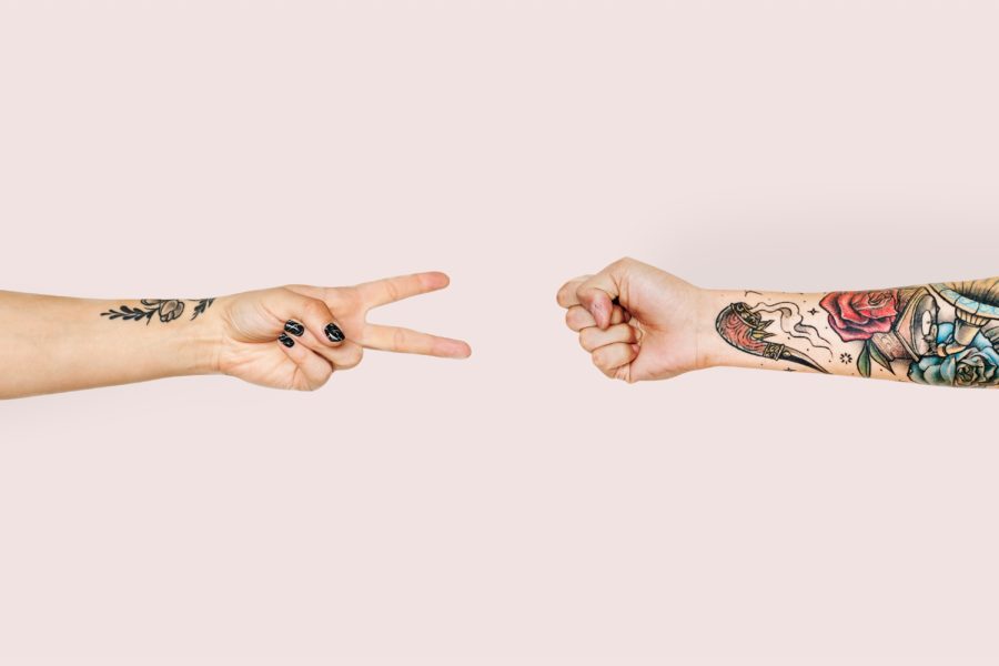 two hands play rock paper scissors against a pink background