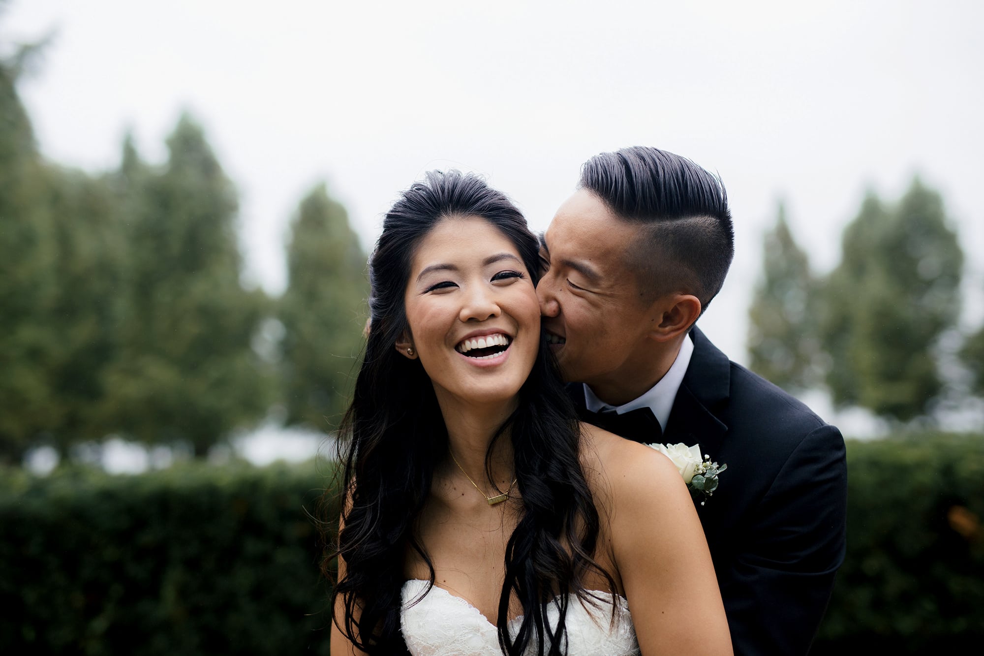 a groom kisses a bride's cheek; they smile