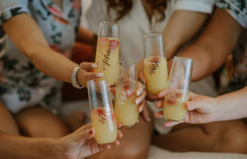 Women in floral robes toasting mimosas in stemless champagne glasses