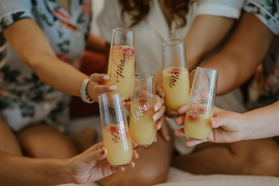 Women in floral robes toasting mimosas in stemless champagne glasses