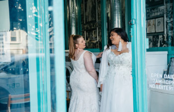 Two women in plus size wedding dresses from Lace & Liberty laughing in a teal doorway