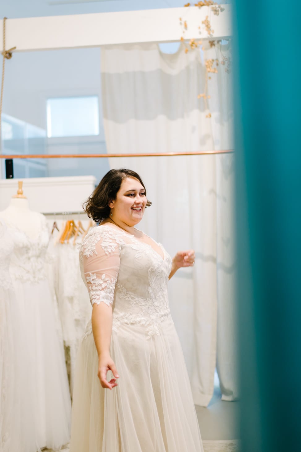 plus size woman in wedding dress smiling at herself in the mirror at Lace and Liberty