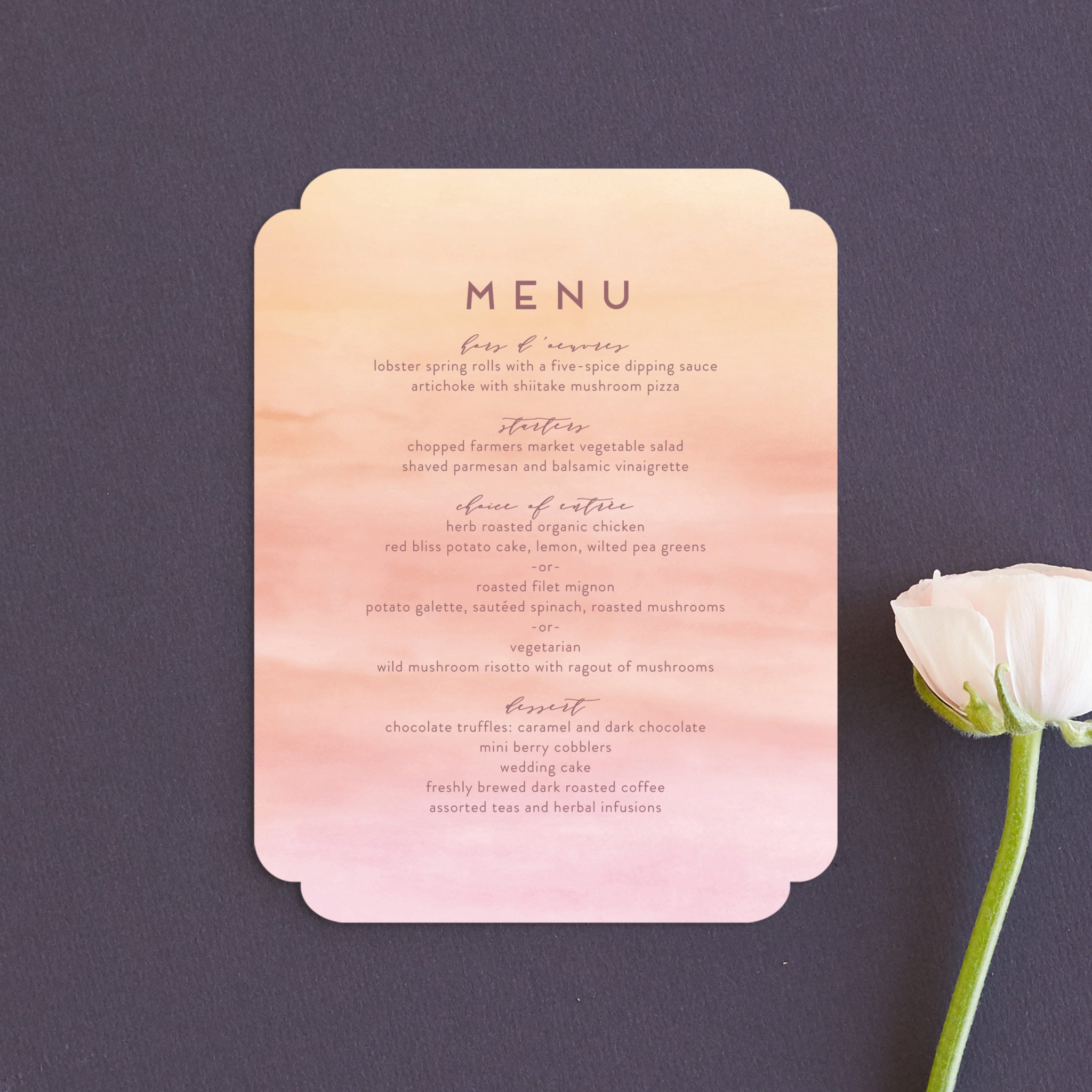 a pink and orange ombre watercolor wedding menu styled on a navy background with a single pink flower slightly out of frame