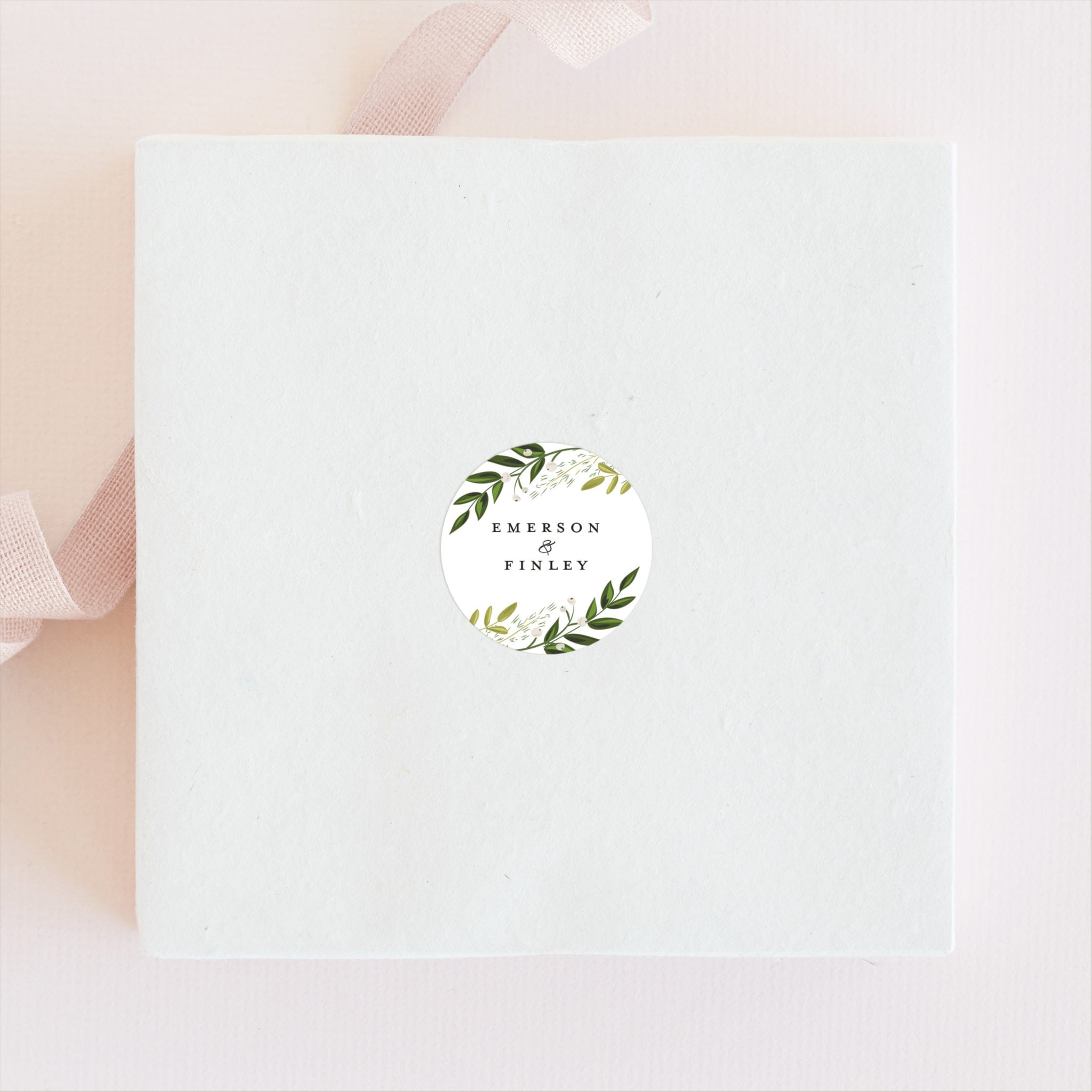 a white box with a sticker on the top featuring olive sprigs styled on a peach backdrop next to a ribbon