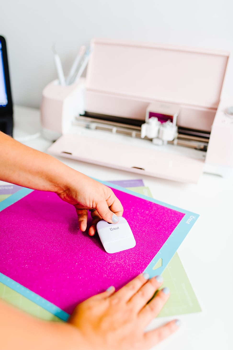A woman tightly adhering her pink paper to the Cricut Explore Air 2 Machine from Michael's Weddings cutting background page