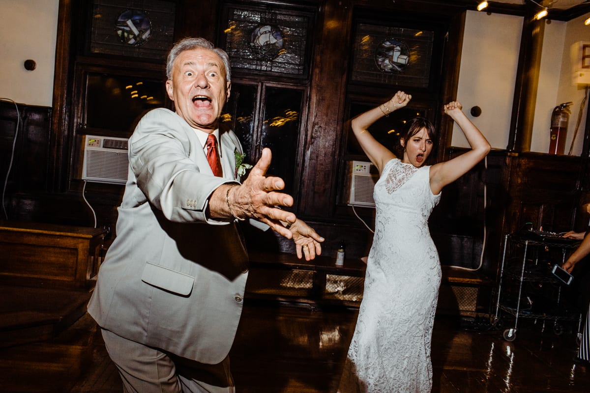 bride and older man are dancing, as he reaches out towards someone in the direction of the camera