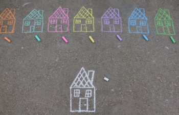 Identical chalk drawings of houses in a row on cement in different colors above a single illustration of a white chalk house
