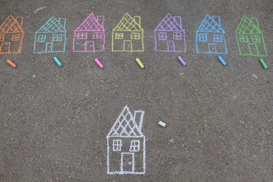 Identical chalk drawings of houses in a row on cement in different colors above a single illustration of a white chalk house