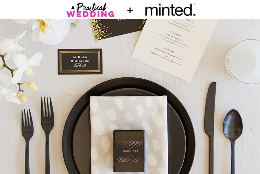 A place setting with a black plate and black flatware with a place card, favor box, and menu from minted. The text "A Practical Wedding + Minted" reads above the image.