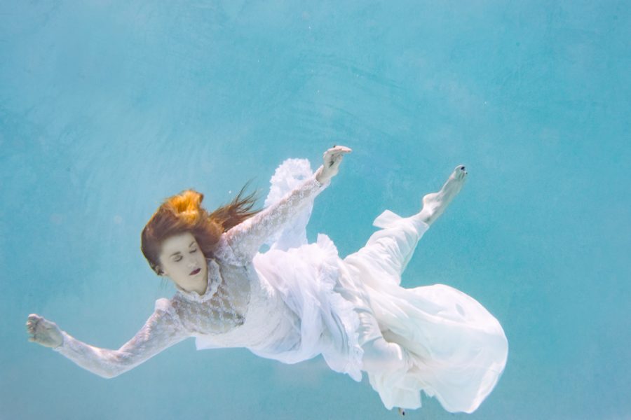 A red-headed woman in a wedding dress, floating, submerged in a blue swimming pool