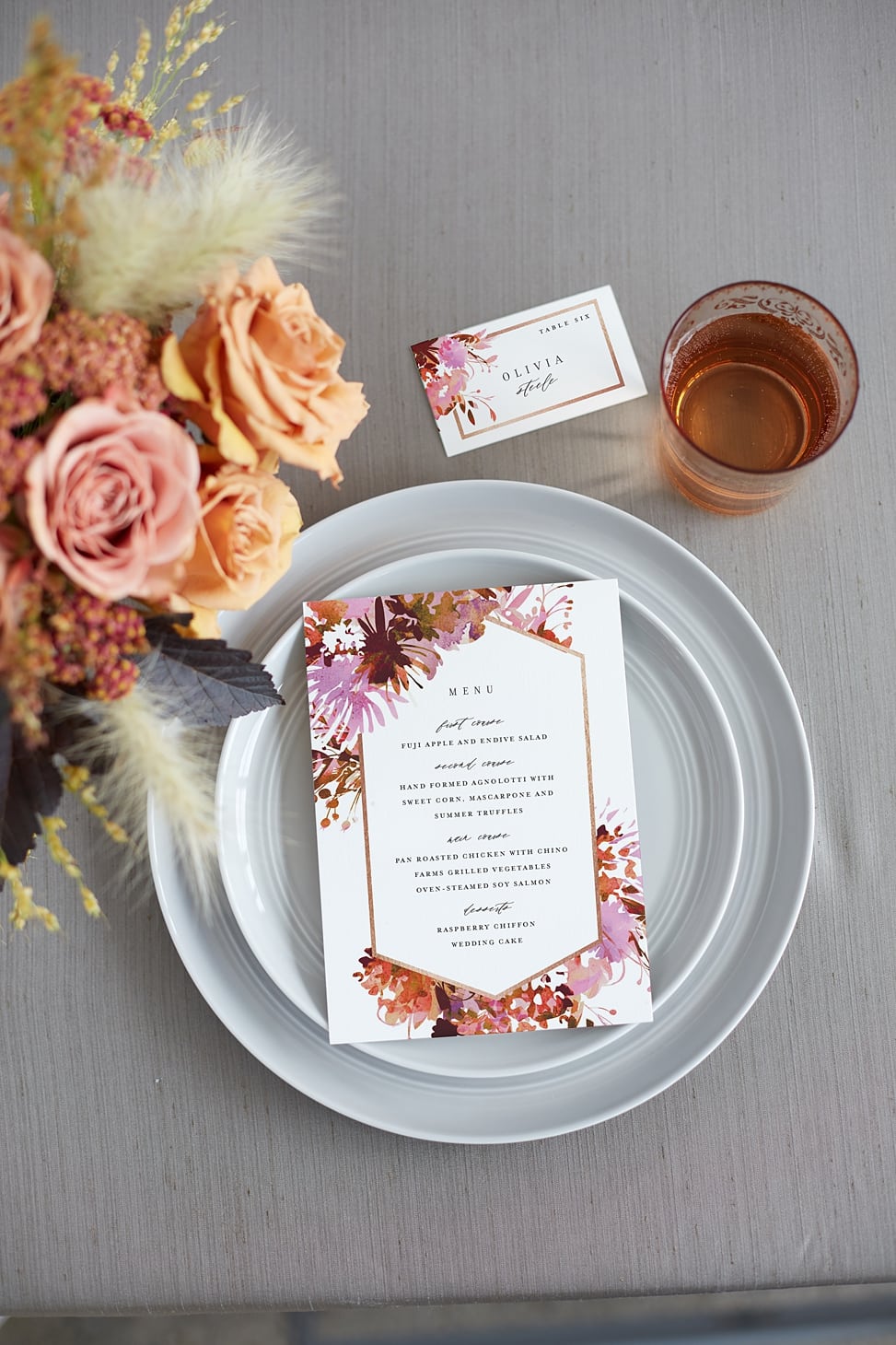 a floral menu and place setting from minted on a gray table cloth with gray plates and peach floral centerpiece