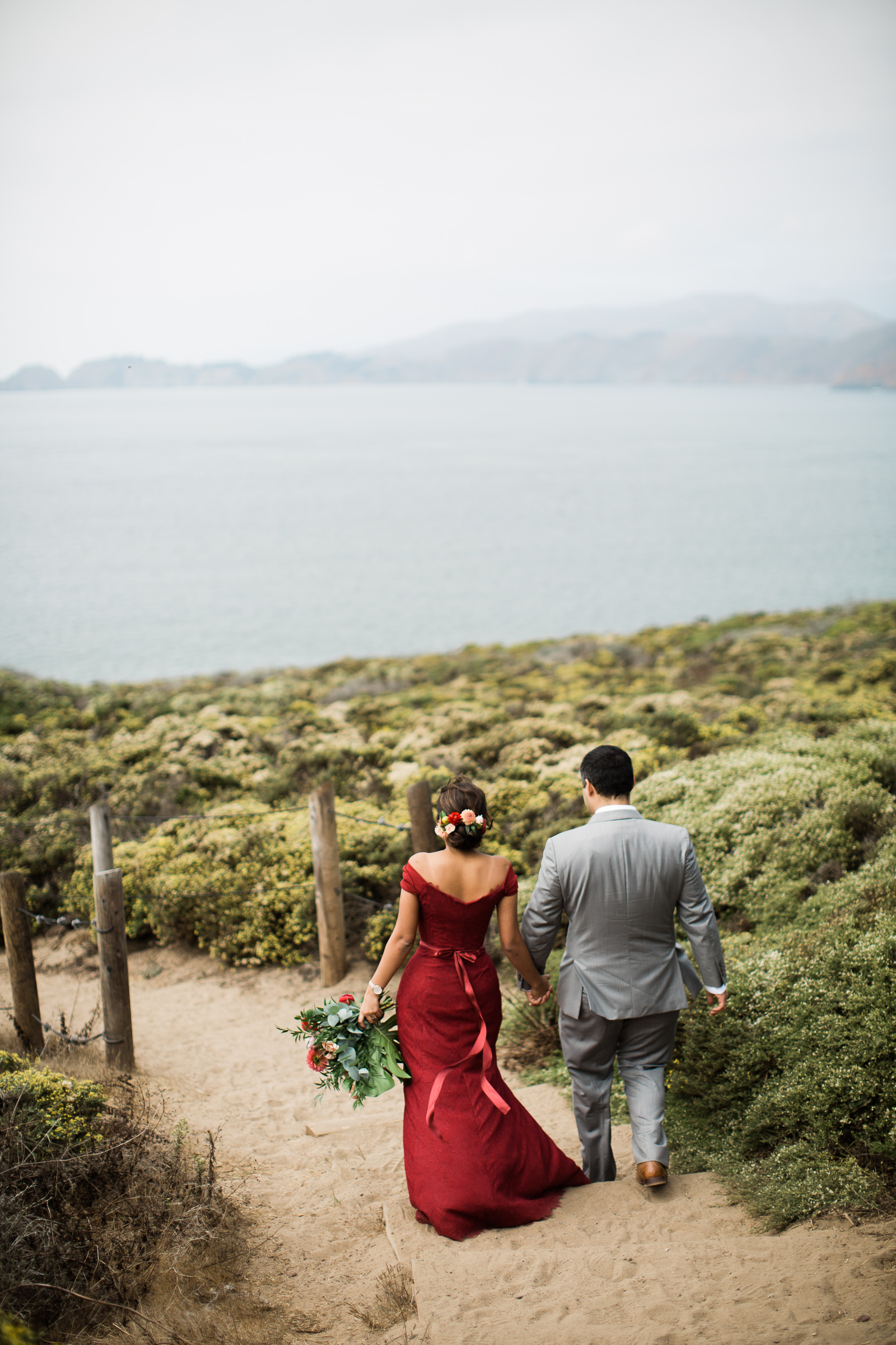 A wedding couple walks down a path towards the ocean in a Manali Anne photo