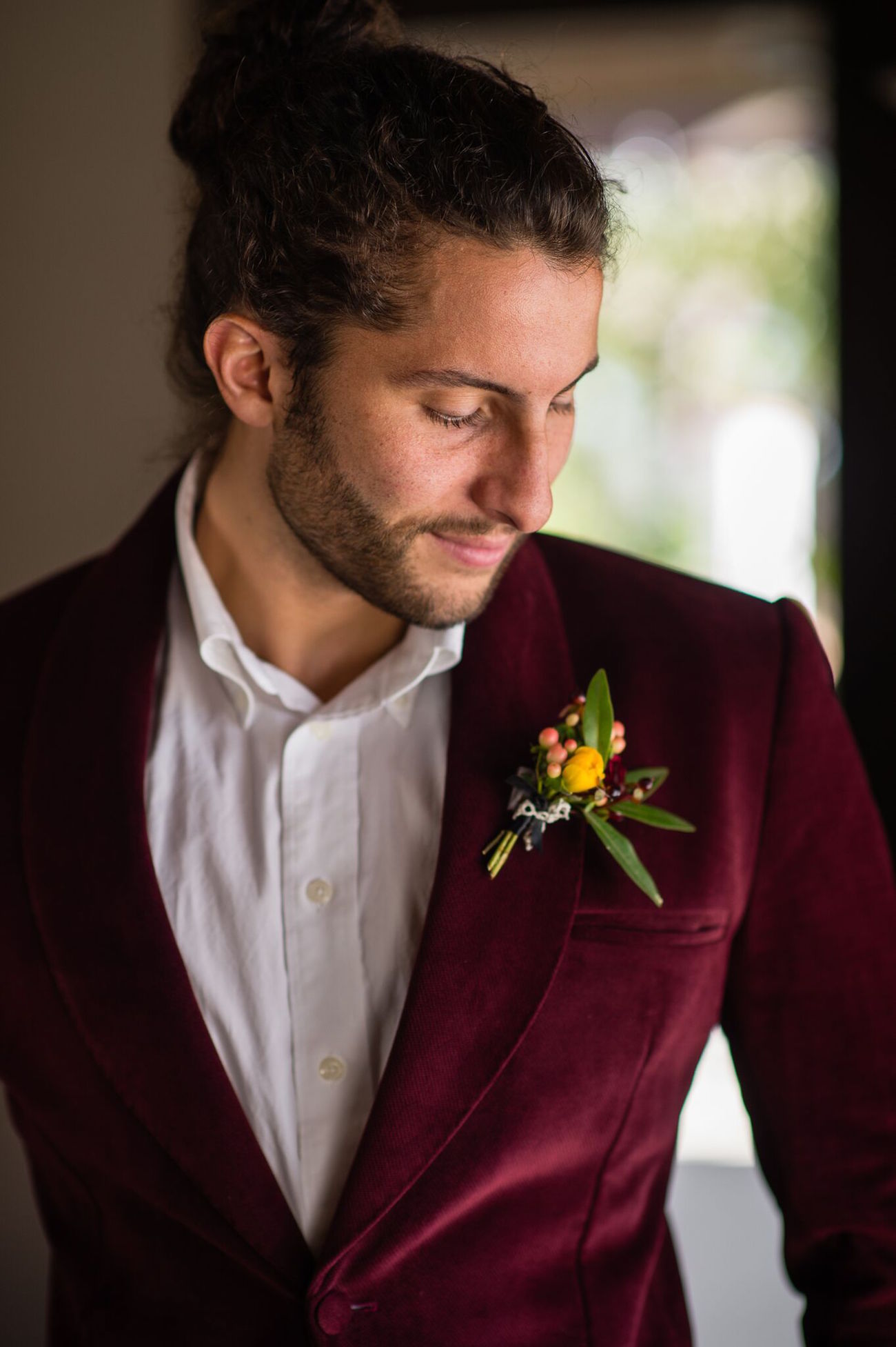 man looking down at boutonnière in his winter wedding colors velvet burgundy coat