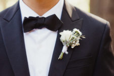 The torso of a man in a black tux with bow tie, wearing a white floral boutonnière.