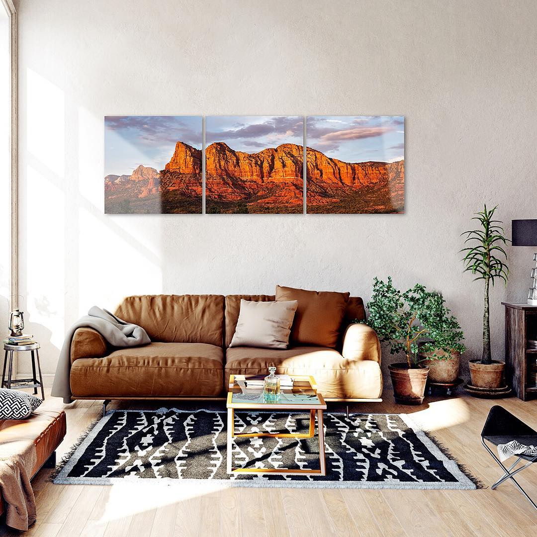 a living room with a large triptych photo hanging over a brown leather couch