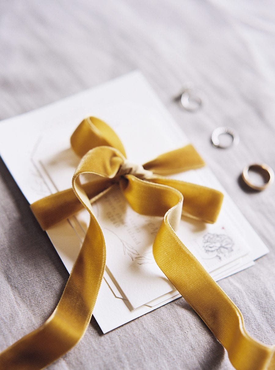 Winter wedding ideas for a gold ribboned invitation set next to rings on a table