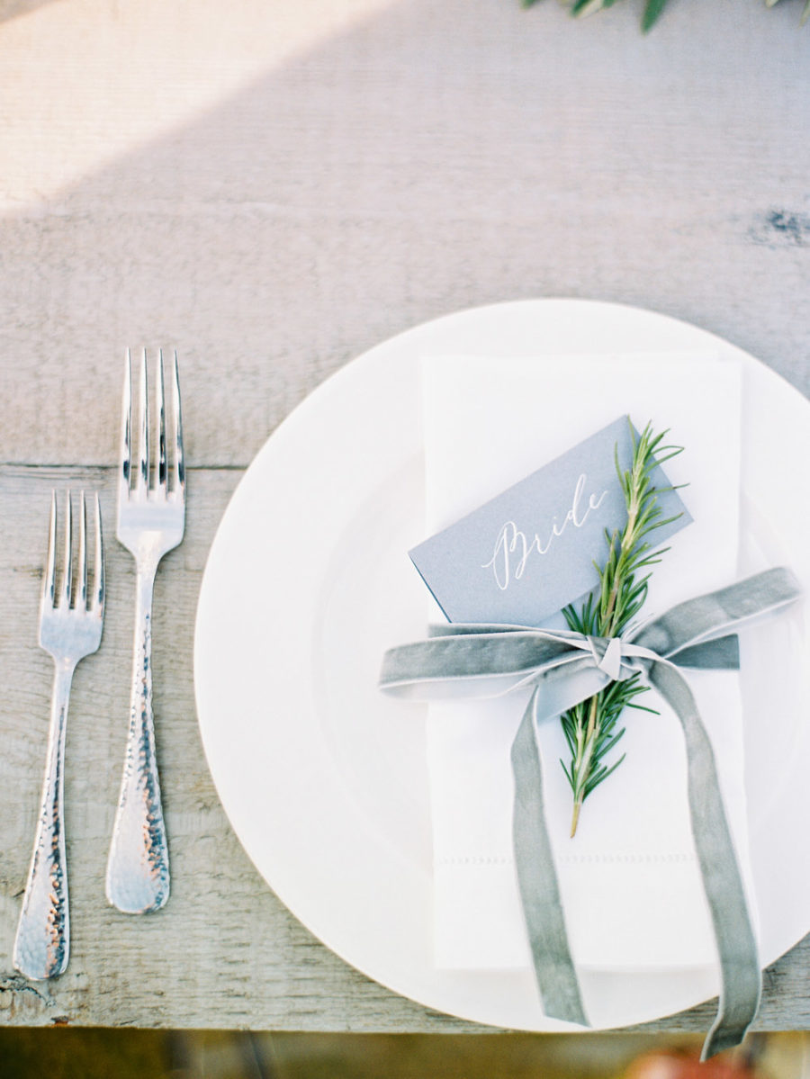 Table setting using winter wedding colors: grey place card, green rosemary sprig, and grey velvet ribbon