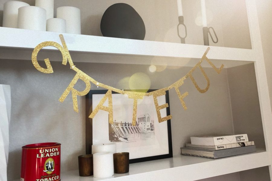 A gold glittery banner reading "Grateful" hangs from a white shelf with candles and books and pictures.