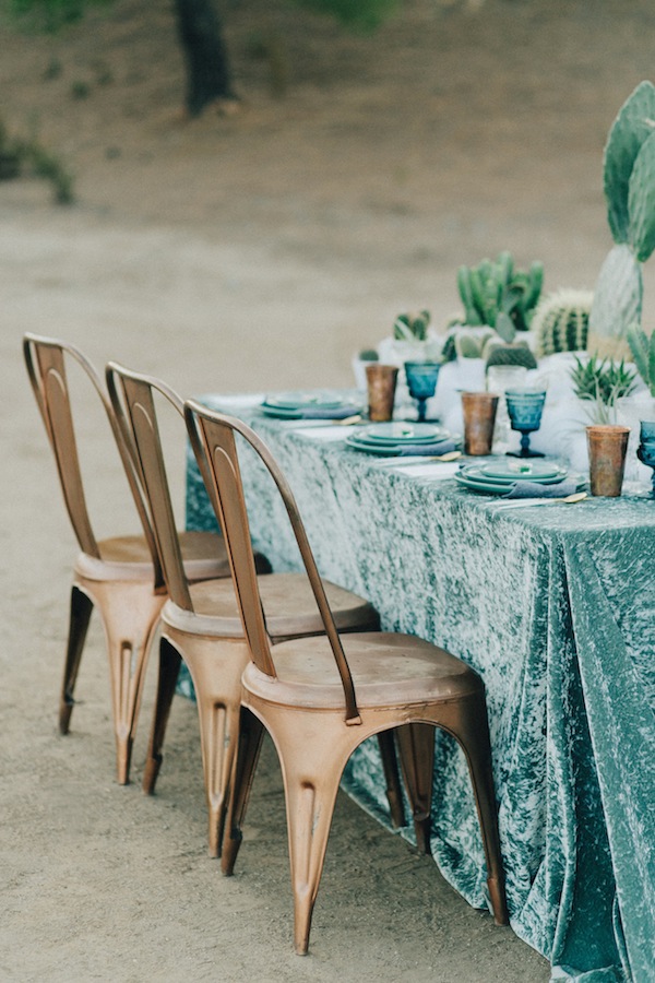 A tablescape in winter wedding colors with brass chairs next to the table, which is covered in a blue velvet tablecloth and fully with coordinating plates 