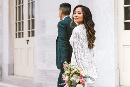 Brunette woman and man walking away, with woman in white cape and dress and holding bouquet