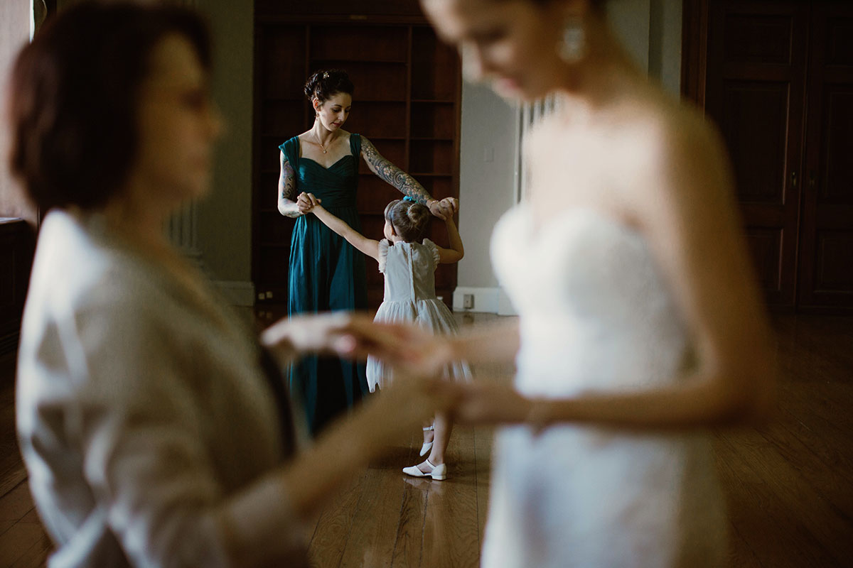 A woman in a green dress and small girl dance behind a bride, who holds hands with an older woman in a Sarah Gormley photo