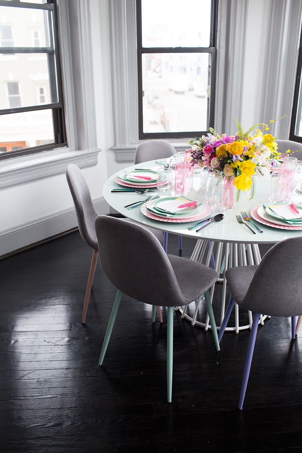 A round table in the bay window of Bureau co-working and event space set for a party with pink chargers and mint place settings with a bright bouquet in the center of the table