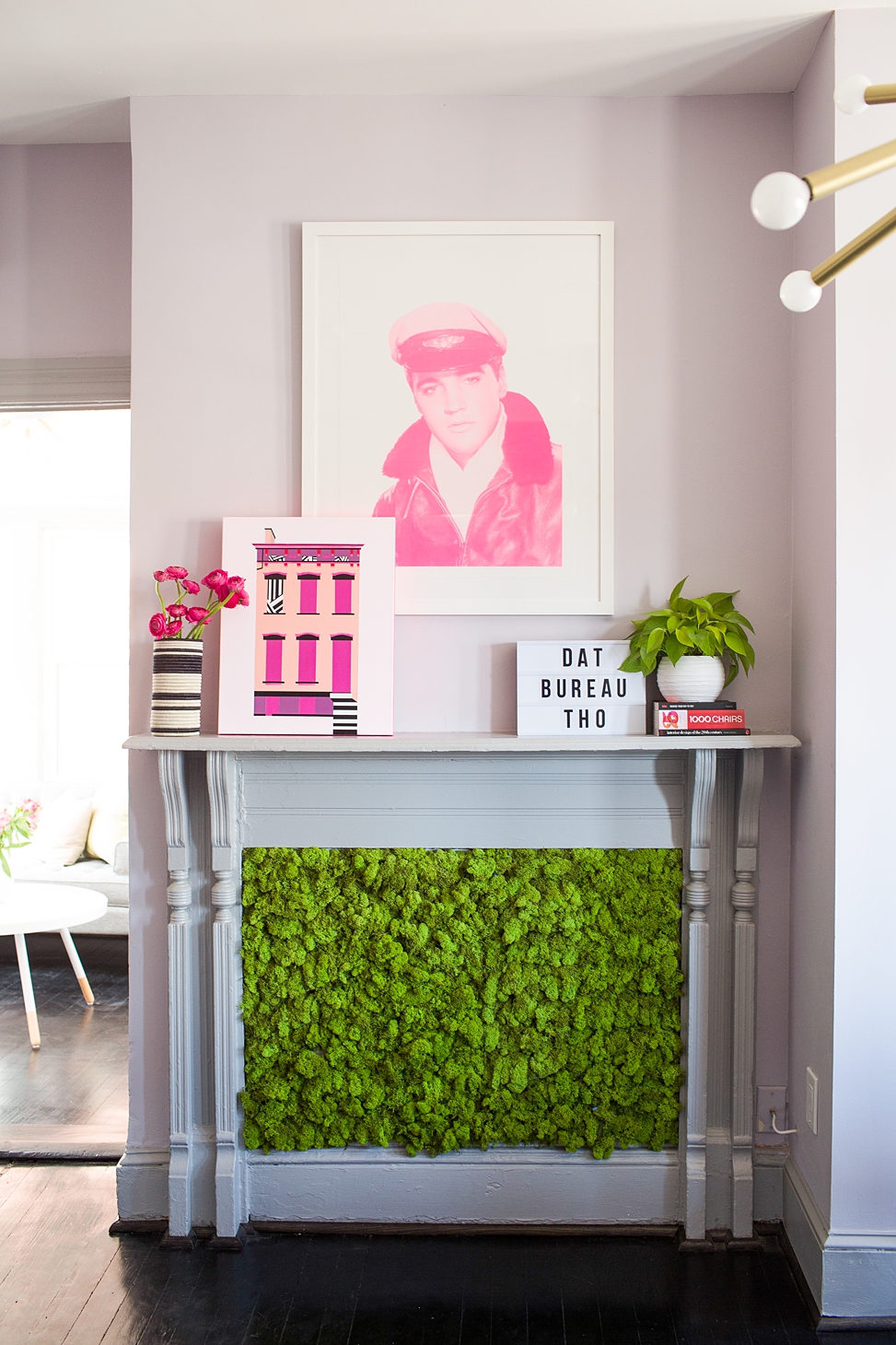 A fireplace with a plant installation at Bureau co-working and event space with a pink print of Elvis hanging above the mantel and other art sitting on the mantel shelf