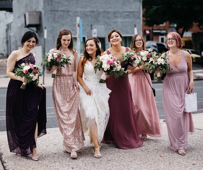 bridal party wearing mismatched david's bridal bridesmaid dresses in shades of pink and wine with sequins and lace