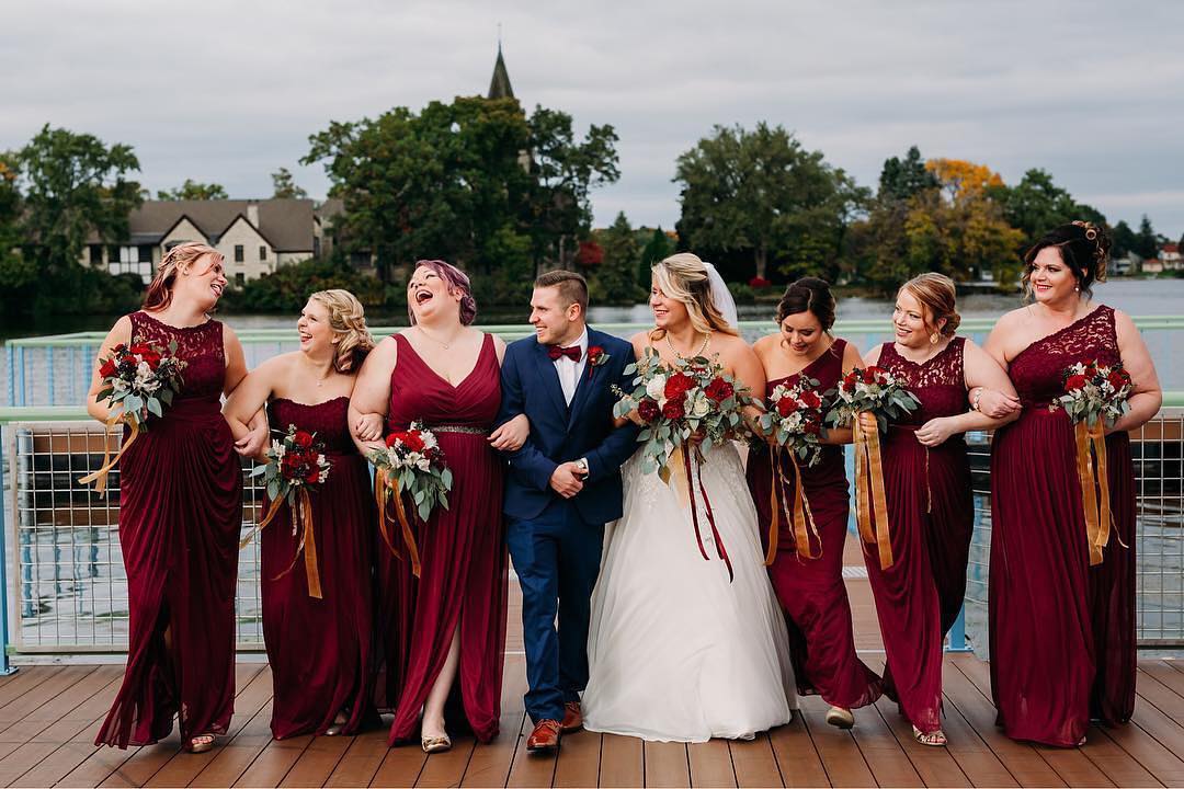 laughing bridal party wearing mismatched oxblood red bridesmaid dresses with lace details and plus size bridesmaids in one shoulder bridesmaid dresses