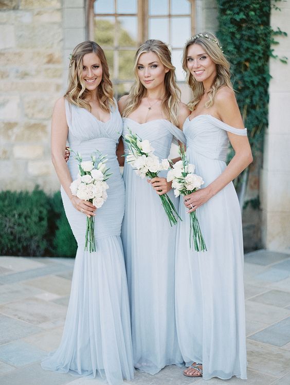 Three women in blue dresses holding bouquets wearing winter wedding colors: icy blue with white bouquets