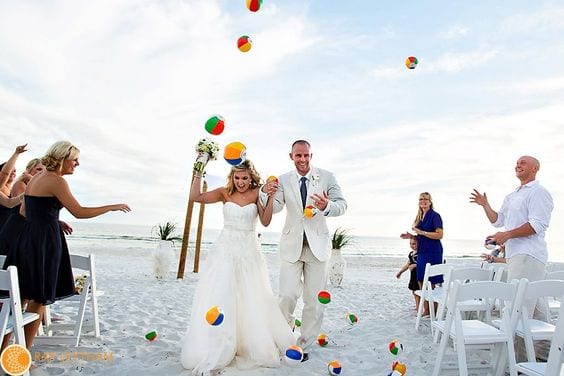 wedding ideas for a couple walking through beach balls guests are throwing at them as the walk back up the aisle at their white-sand beach wedding ceremony