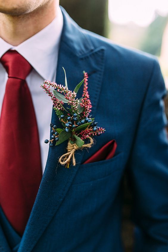 Close up of man in winter wedding colors: a medium blue coat with a dark red tie and coordinating boutonnière