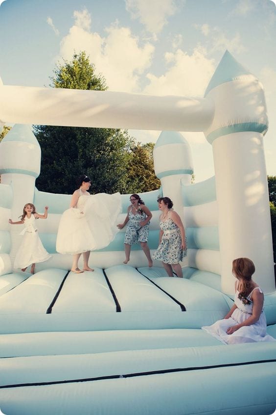 wedding ideas for a bride and bridal party jumping in a light blue and white bouncy castle