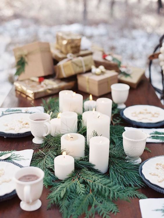 tablescape in winter wedding colors: white candle and fir table runner among dishes with blue accents and a pile of gold and kraft-wrapped gifts