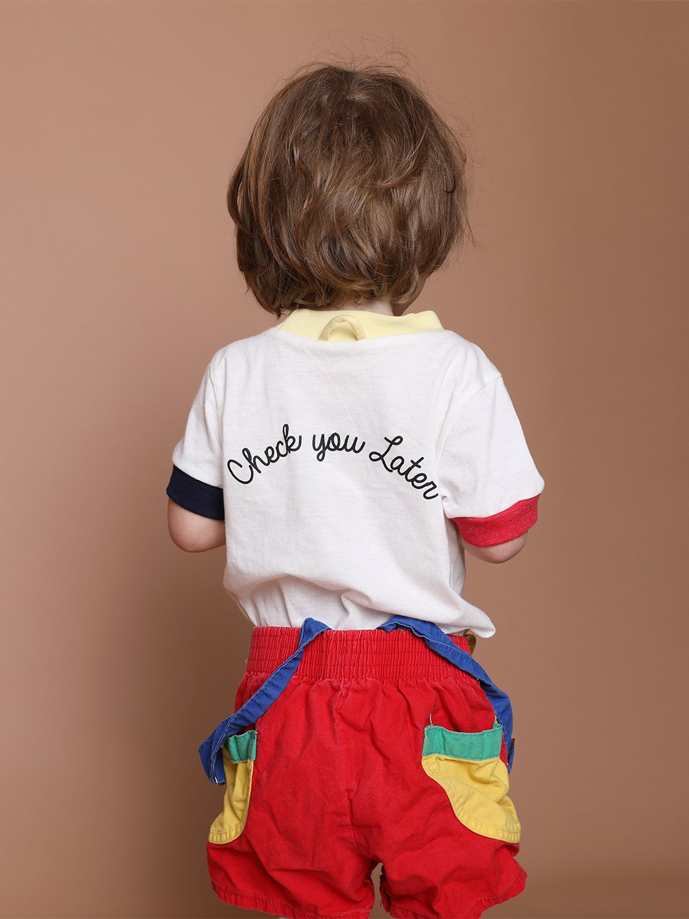 Kid with their back facing towards the camera wearing a shirt embroidered with the phrase check you later