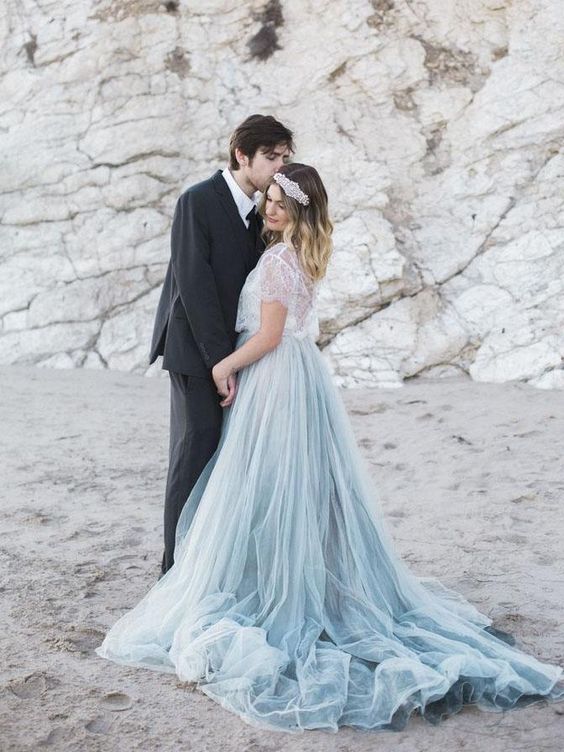 A man in a black suit kisses a woman on the beach; she is wearing winter wedding colors: a blue tulle skirt with a white lace top and silver hairpiece