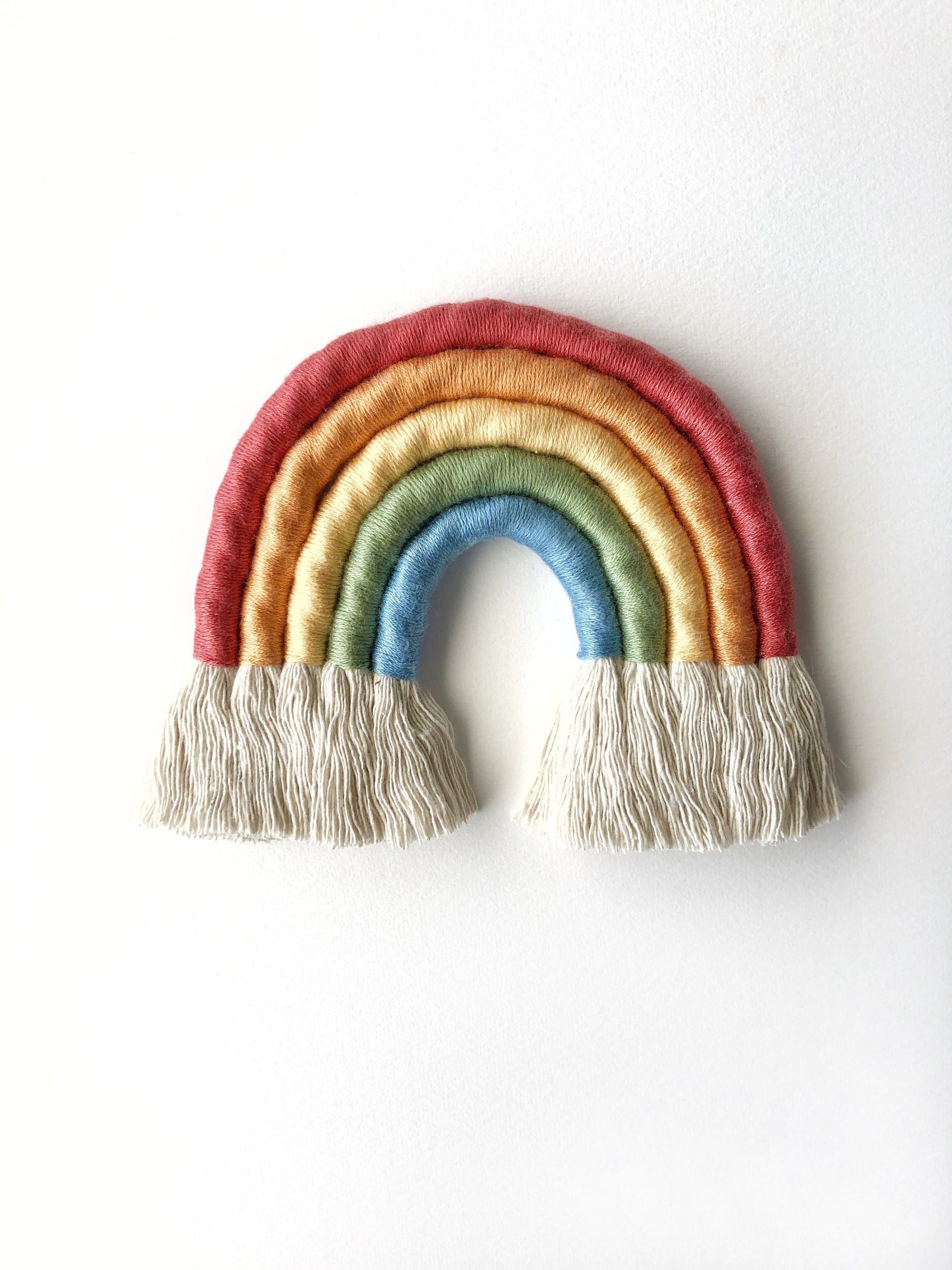 rainbow wall hanging with white fringe clouds hanging on a white wall