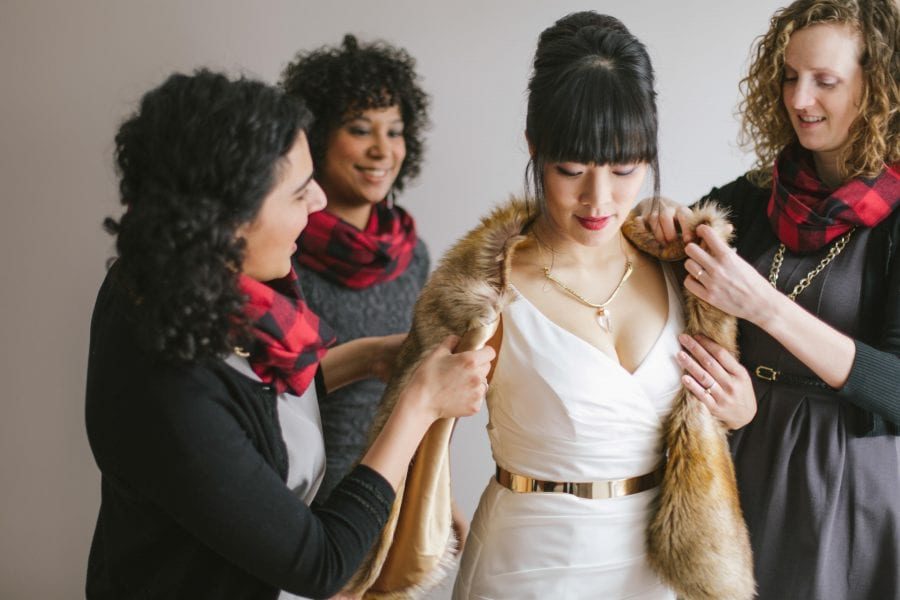 Winter wedding ideas for a woman who is being helped into a fur stole by three other women