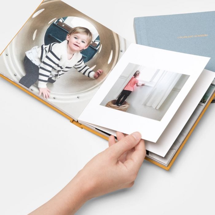 someone holding a photo album open on top of another linen bound photo album
