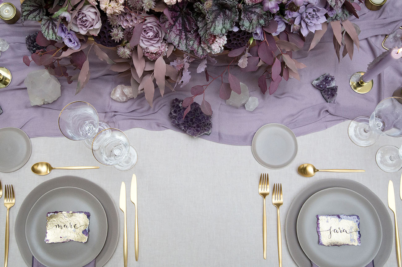Place setting in winter wedding colors: gray plates with lavender table runner, gold flatware, and amethyst accents
