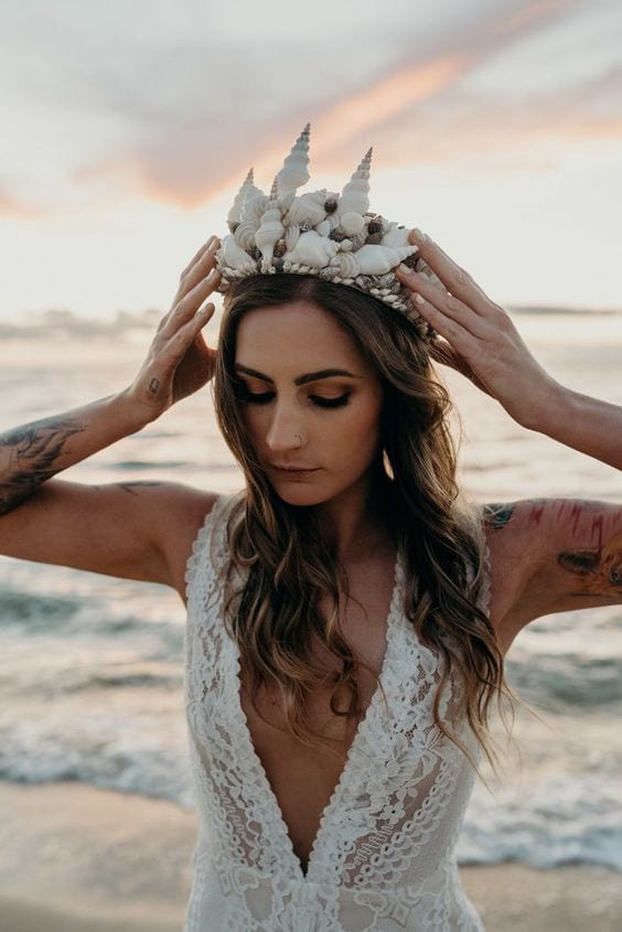 wedding ideas for headpiece—woman wearing a shell crown in a wedding dress with waves crashing behind her as the sun sets