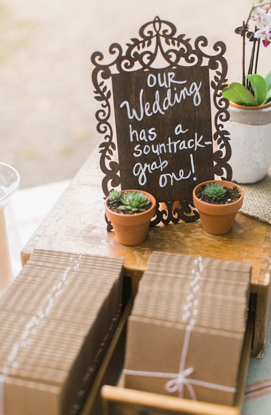 Wedding ideas for a wedding soundtrack—chalkboard sign that reads "Our Wedding has a soundtrack—grab one!" above rows of cds packaged in kraft