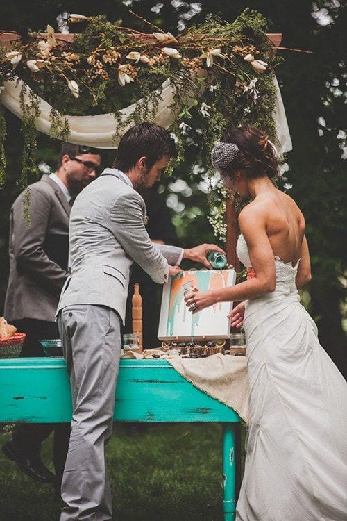 wedding ideas for a couple making a painting during their wedding ceremony by pouring two colors of paint down the top of a canvas